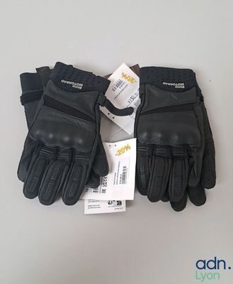 une paire de gants en cuir noir, encore étiquetés, posée sur une table
