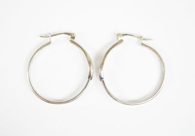 une paire de boucles d'oreilles créoles en argent sur fond blanc