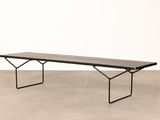a black bench sitting on top of a cement floor next to a white wall