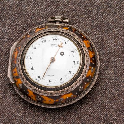 un gros plan d'une montre de poche posée sur une surface marron