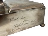 an old silver box with writing on it sitting on a white surface