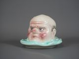 une petite figurine en céramique représentant un homme dont le visage est sculpté sur une soucoupe