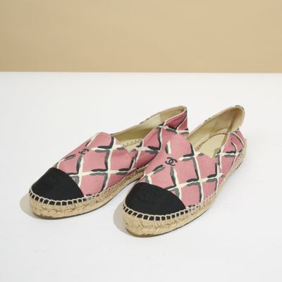 une paire d'espadrilles roses et noires posées sur une surface blanche