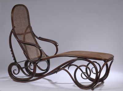 un vieux fauteuil à bascule avec une assise et un repose-pieds en bois, posé sur une surface blanche