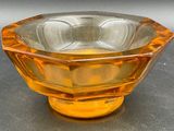un saladier en verre orange posé sur une table, sur fond gris