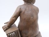 statue of a child sitting on a chair with a basket in his lap