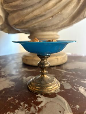 a blue glass bowl on a table with a statue in the background