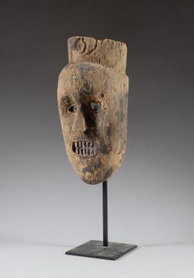 un masque en bois posé sur un socle, devant un fond gris