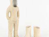 une petite statue représentant un homme debout à côté d'une paire de bottes