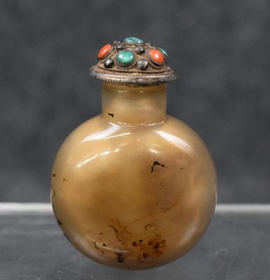 un petit vase en verre avec un couvercle en argent, posé sur une table