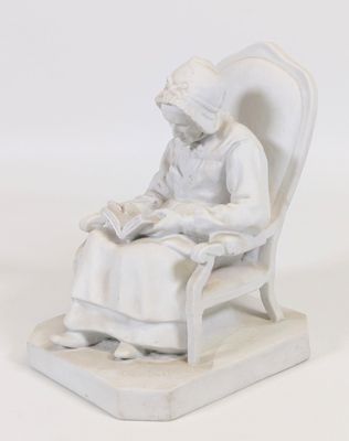 une statue représentant une femme assise sur une chaise en train de lire un livre