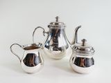 three pieces of silver tea and coffee set on a white surface