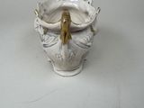 a white vase with a gold handle on a white table