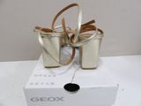 silver and gold high heeled sandals with a bow on top of a box