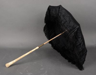 un vieux parapluie noir avec un manche en bois posé sur une surface grise
