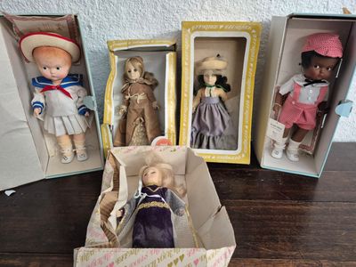 Plusieurs poupées sont rangées dans des boîtes posées sur une table, avec un mur en arrière-plan.