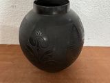 un vase noir posé sur une table, avec un mur blanc en arrière-plan