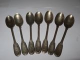 six silver spoons are lined up on a white surface