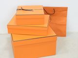 trois boîtes orange empilées les unes sur les autres, avec un sac en papier kraft
