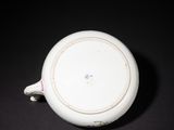 a small white bowl with a handle on a black surface