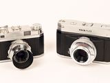 two cameras sitting next to each other on a white surface