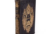 an old book with a gold and black cover sitting on a white surface