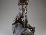 statue en bronze représentant un homme assis sur un rocher, les bras levés