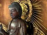 a statue of a buddha holding a staff in front of a golden wall