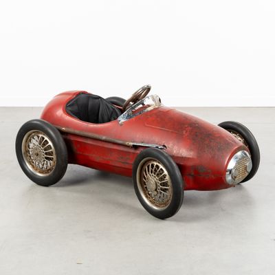 an old red toy car sitting on top of a cement floor