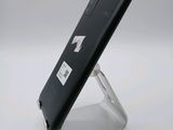 the back of a black cell phone on a stand on a white surface