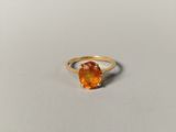a close up of a ring with an orange stone on a white surface