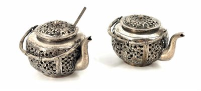 two silver teapots sitting next to each other on a white surface