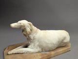 sculpture représentant un chien blanc couché sur une planche de bois, sur fond gris