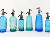 six bouteilles en verre bleues sont alignées sur une surface blanche