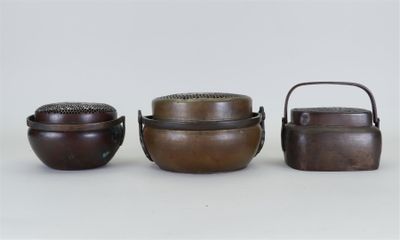 trois petits récipients métalliques munis de poignées, posés sur une surface blanche