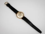 une montre en or avec un bracelet en cuir noir et un cadran blanc