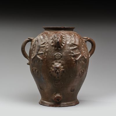 un vieux vase marron muni d’anses, sur un fond gris