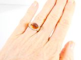 a woman ' s hand holding a ring with a brown stone