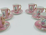 six tasses à café roses et dorées avec leurs soucoupes, posées sur une table blanche