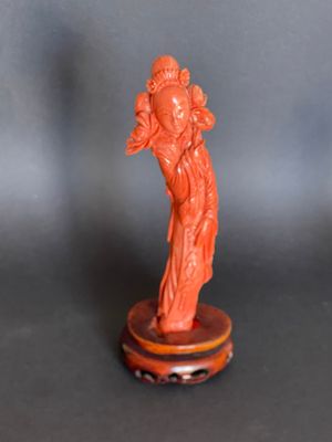 une statue orange représentant une femme tenant un bébé dans ses bras, posée sur un socle en bois