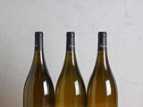 trois bouteilles de vin posées sur une table en bois, à côté d'une bouteille de vin
