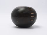 une boule noire percée de trous, posée sur une surface blanche
