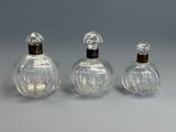 three clear glass perfume bottles with wooden lids on a gray surface