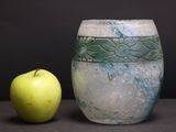 a green apple sitting next to a vase on a table