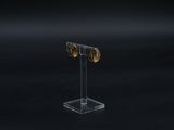 a close up of a pair of gold earrings on a clear stand