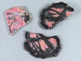 trois morceaux de roche rose et noire posés sur une surface blanche