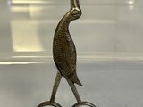 a metal bird that is sitting on top of a pair of scissors