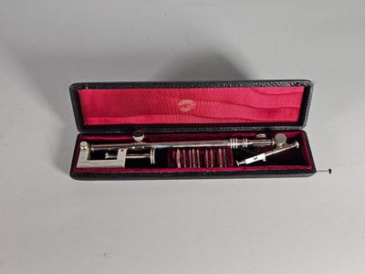 un instrument argenté et rouge dans un étui posé sur une surface blanche