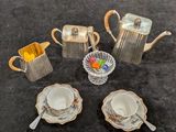 une théière en argent, des tasses et des soucoupes posées sur une table