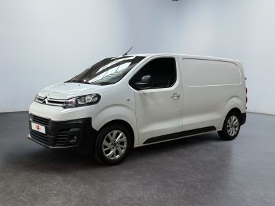 La camionnette blanche est garée dans une grande pièce au sol noir.
